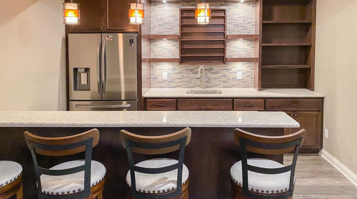 A finished basement bar renovation in a modern home, complete with gray marble countertops and dark wood